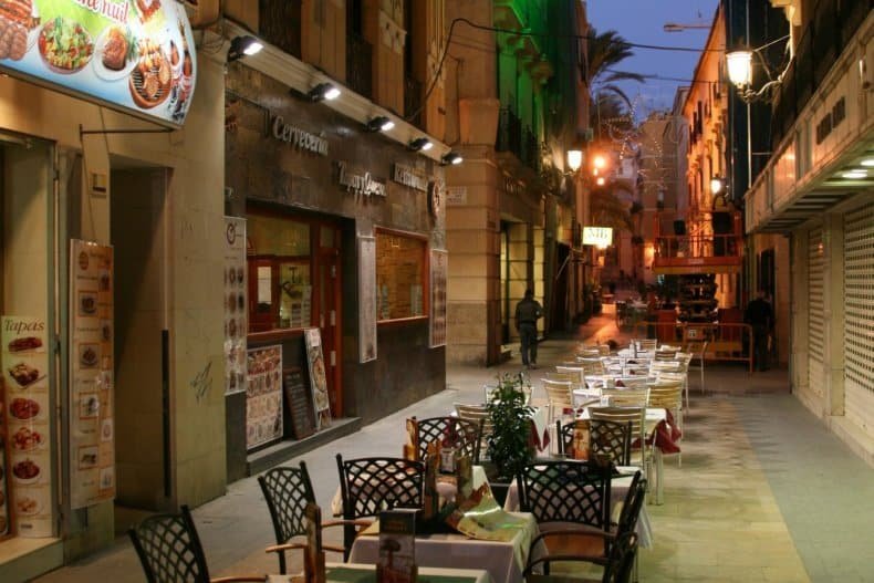 Zonnig terras in het centrum van Alicante met mensen die genieten van eten en drinken tussen Spaanse gebouwen